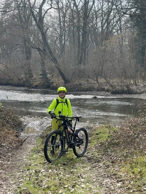 川のほとりで自転車を握る黄色いジャケットを着た男性